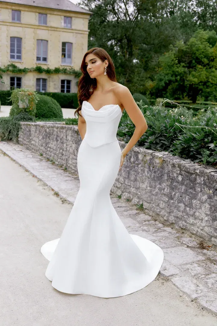 A woman in a white wedding dress is standing on a sidewalk in front of a building.