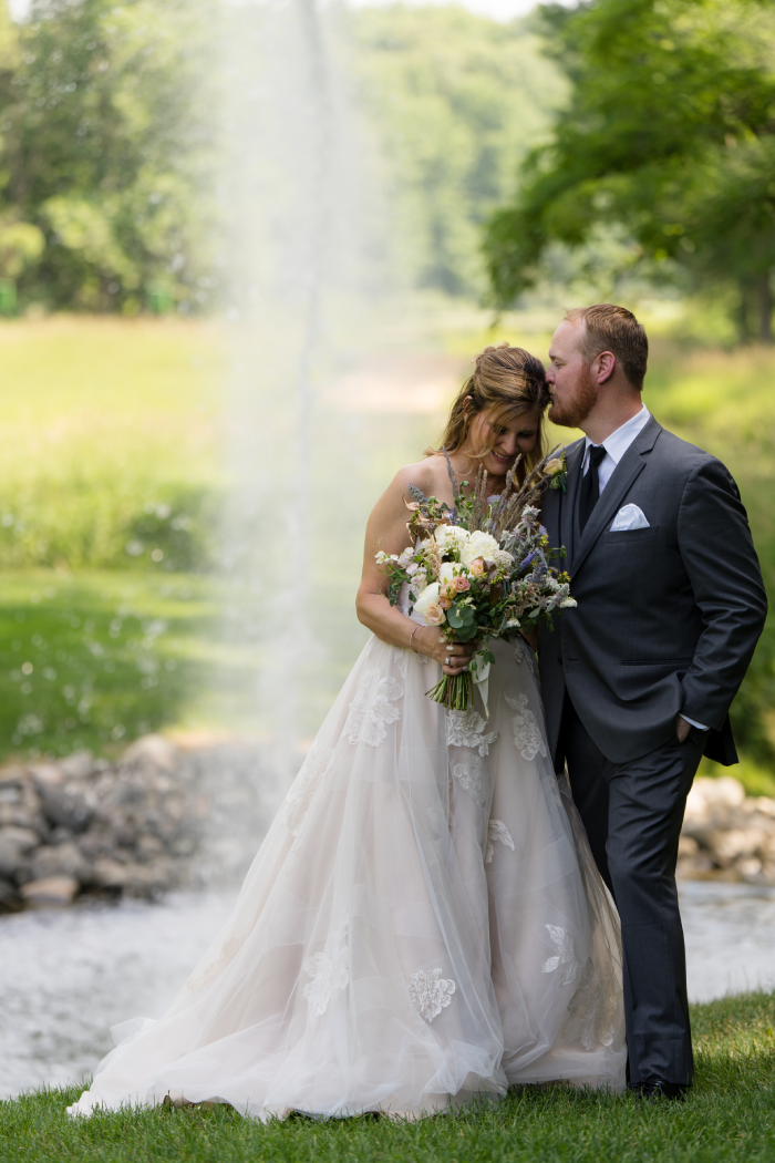 A bride and groom are posing for a picture in front of a fountain.