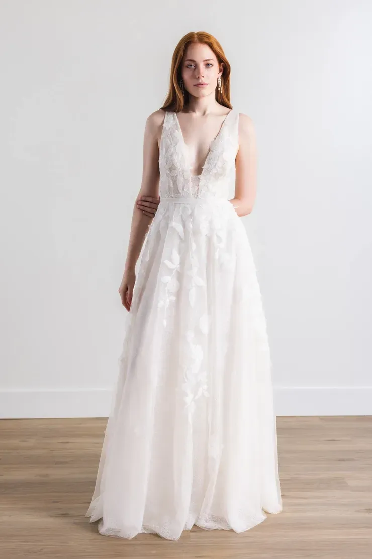 A woman in a white wedding dress is standing on a wooden floor.