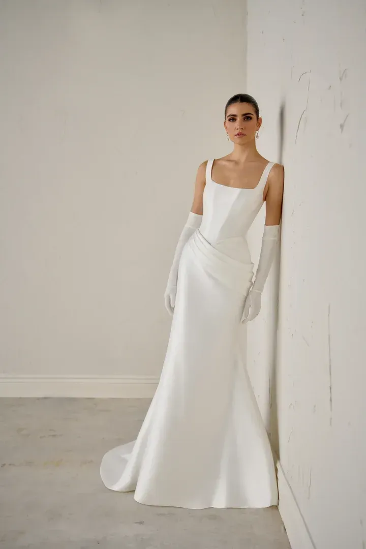 A woman in a white wedding dress is standing in front of a wall.