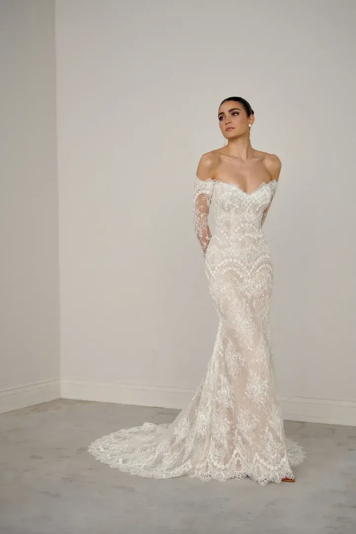 A woman in a white wedding dress is standing in front of a wall.