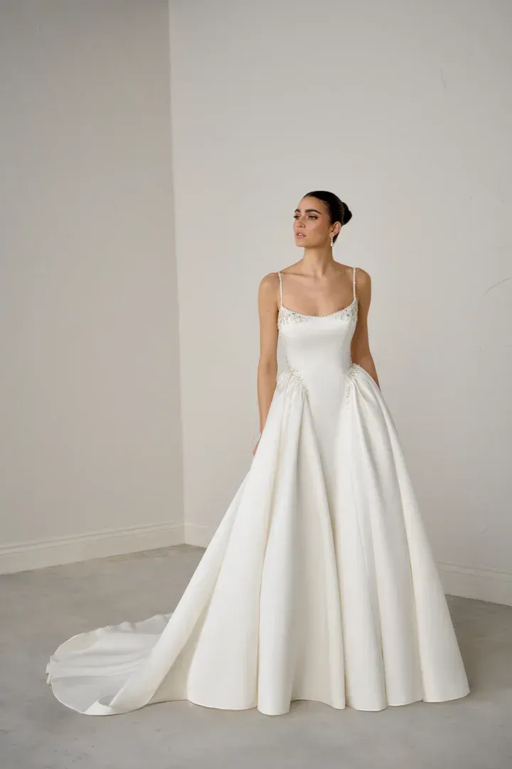 A woman in a white wedding dress is standing in front of a wall.