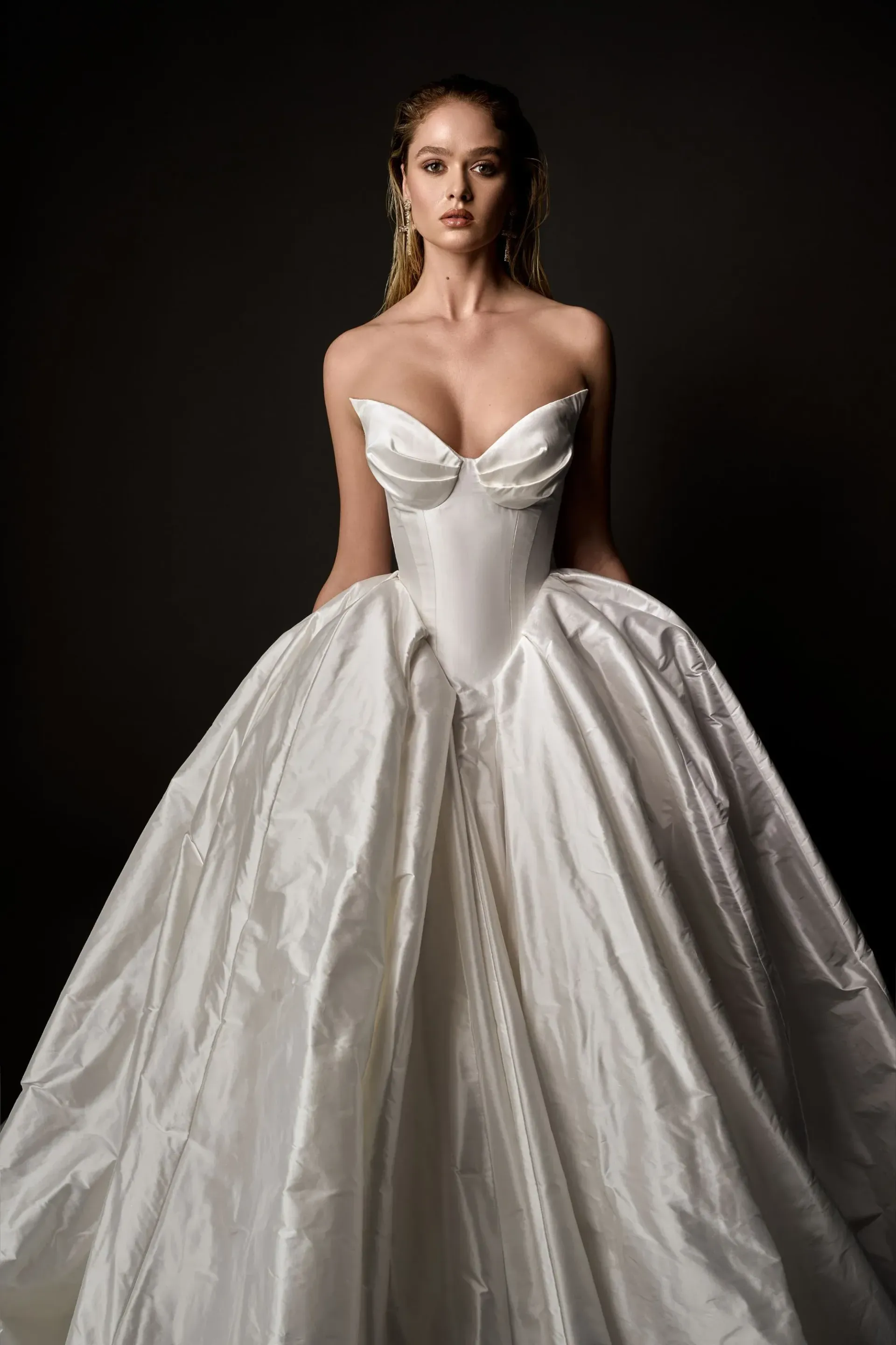 Woman wearing a white, strapless ball gown, posing in front of a dark background.