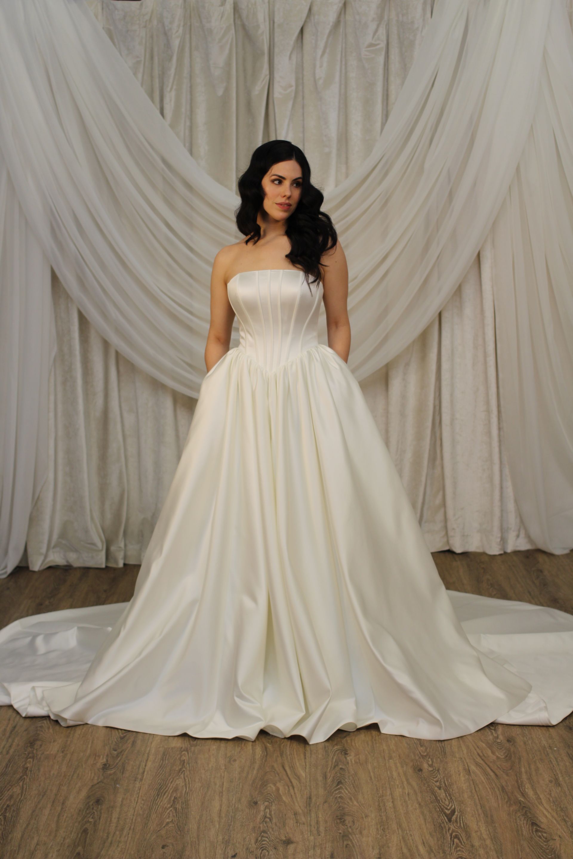 Woman in a strapless ivory satin ball gown with pearl accents and elbow-length gloves.