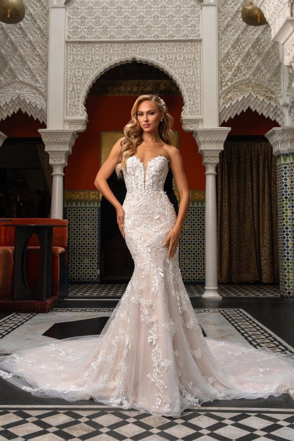 Woman in a strapless white wedding dress with floral embellishments, posing in a decorative arched courtyard.