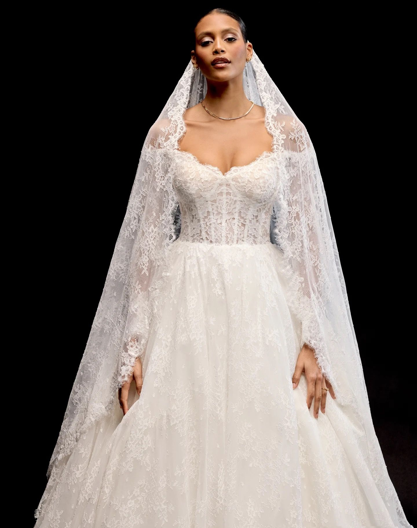 A woman in a white wedding dress is standing in front of a wall.