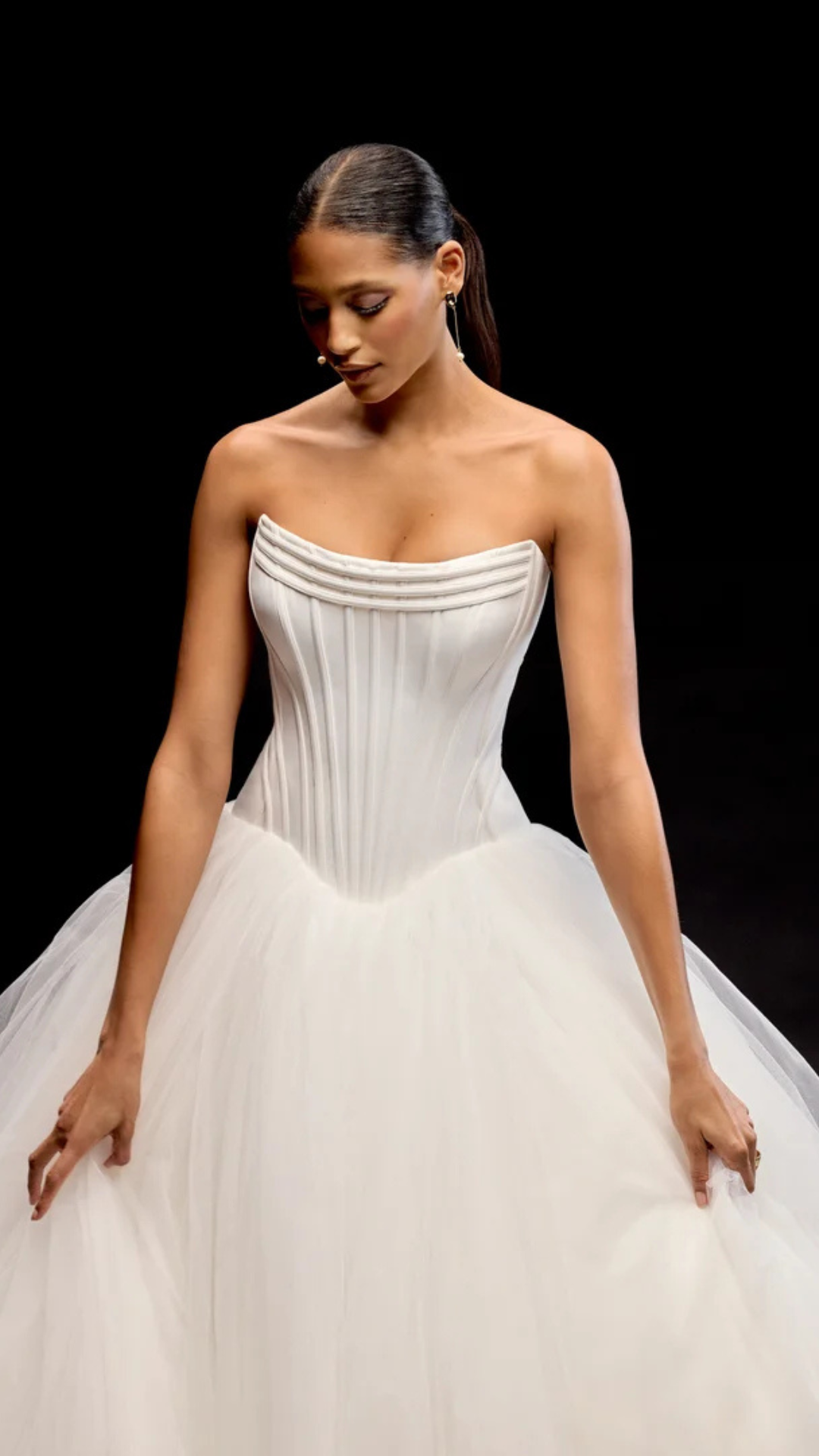 Woman in a white strapless wedding gown, looking down. Black background.