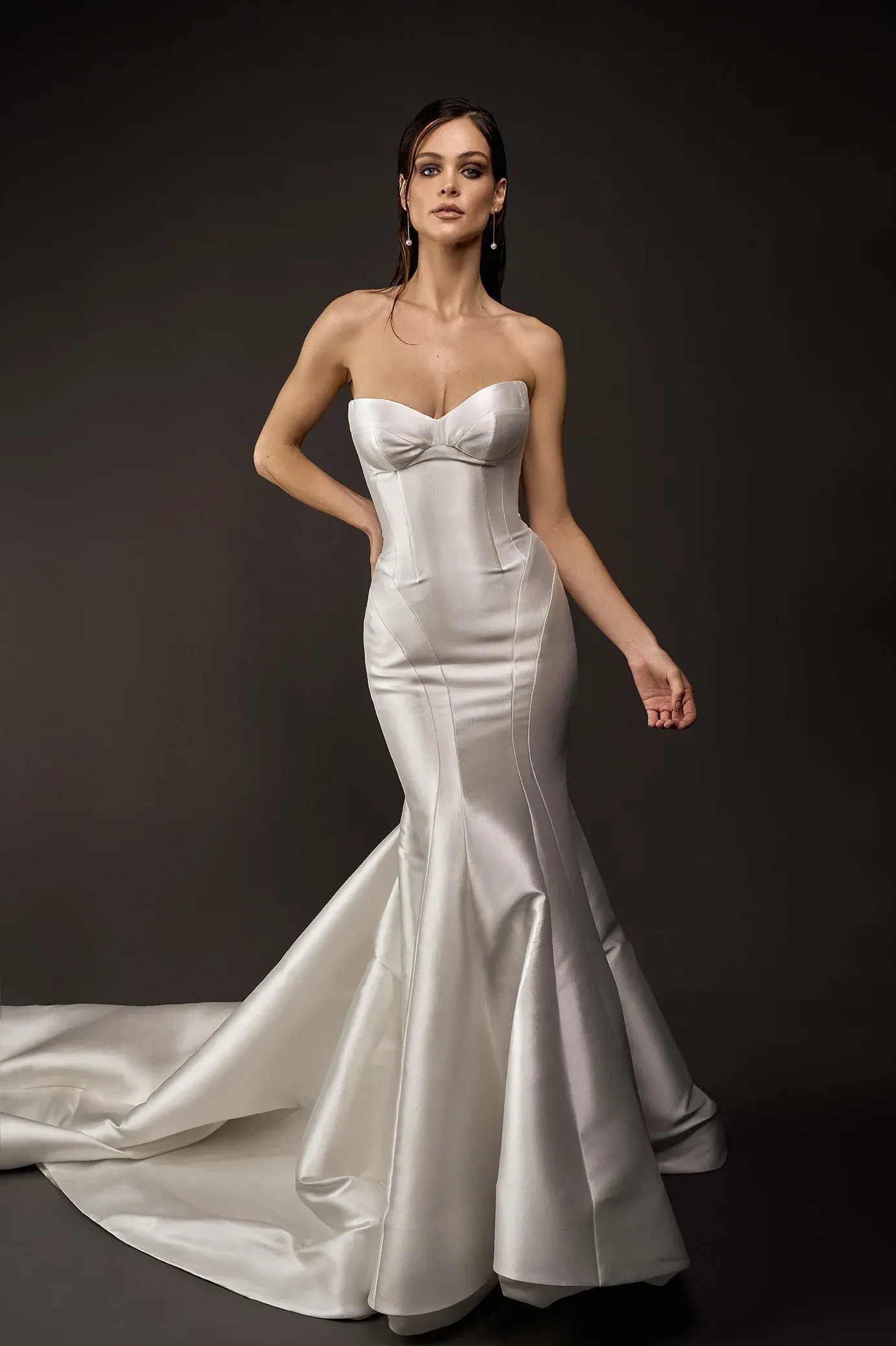 Woman in a white strapless mermaid wedding dress with a long train, dark background.