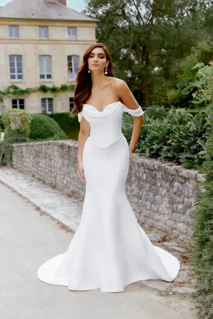 Woman in white off-the-shoulder wedding gown poses outdoors.