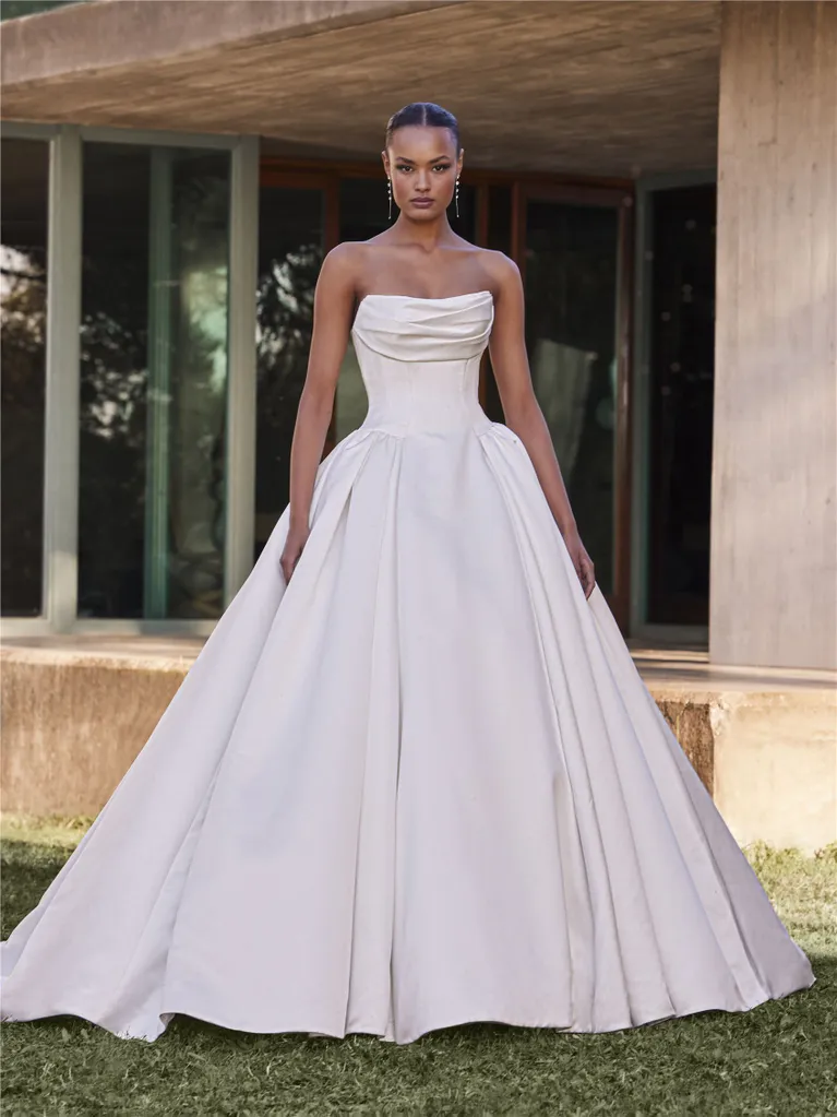 Woman in strapless white ballgown stands outdoors.