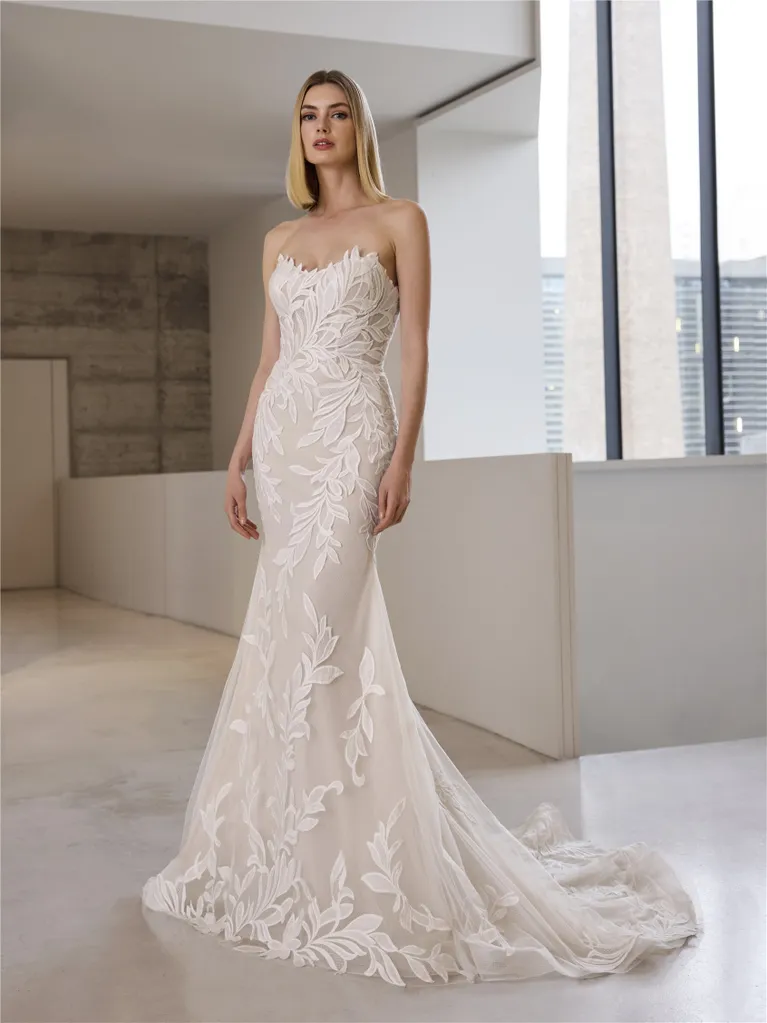 Woman in strapless lace wedding dress with a train, standing in a modern building.