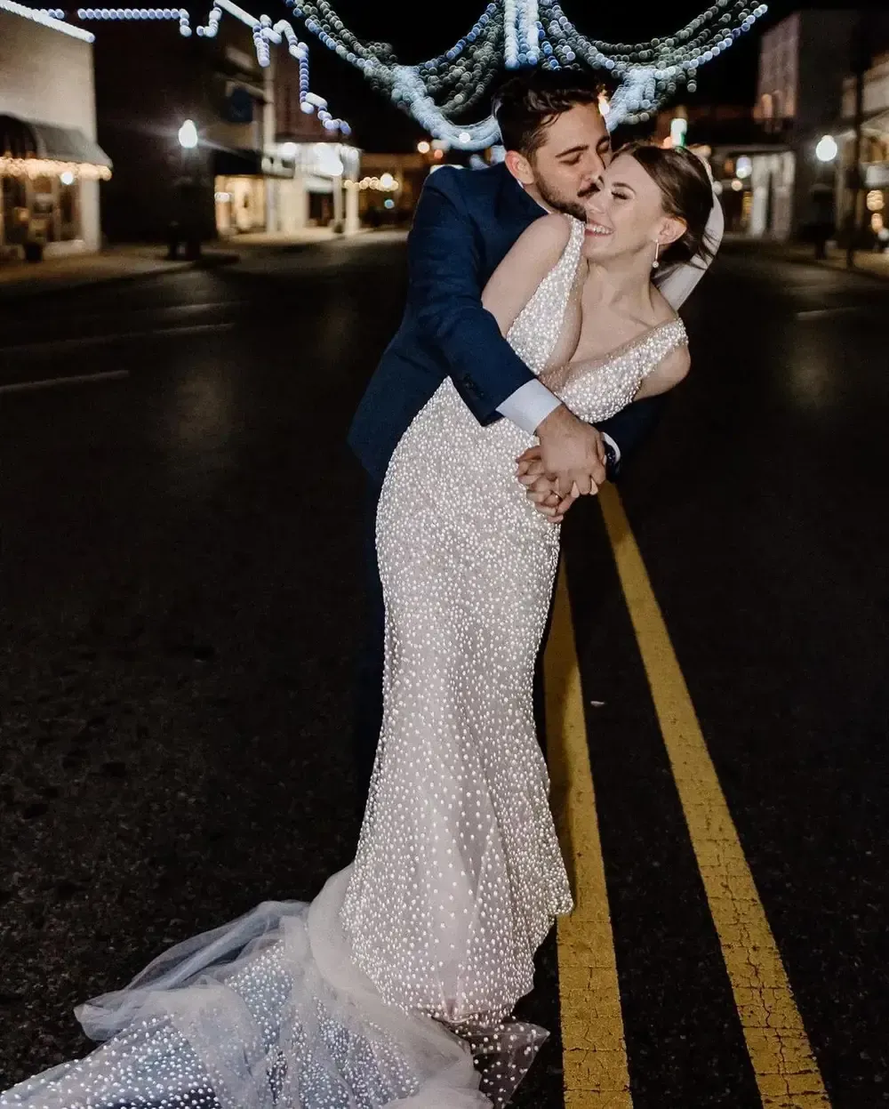 A bride and groom are kissing on the street at night.