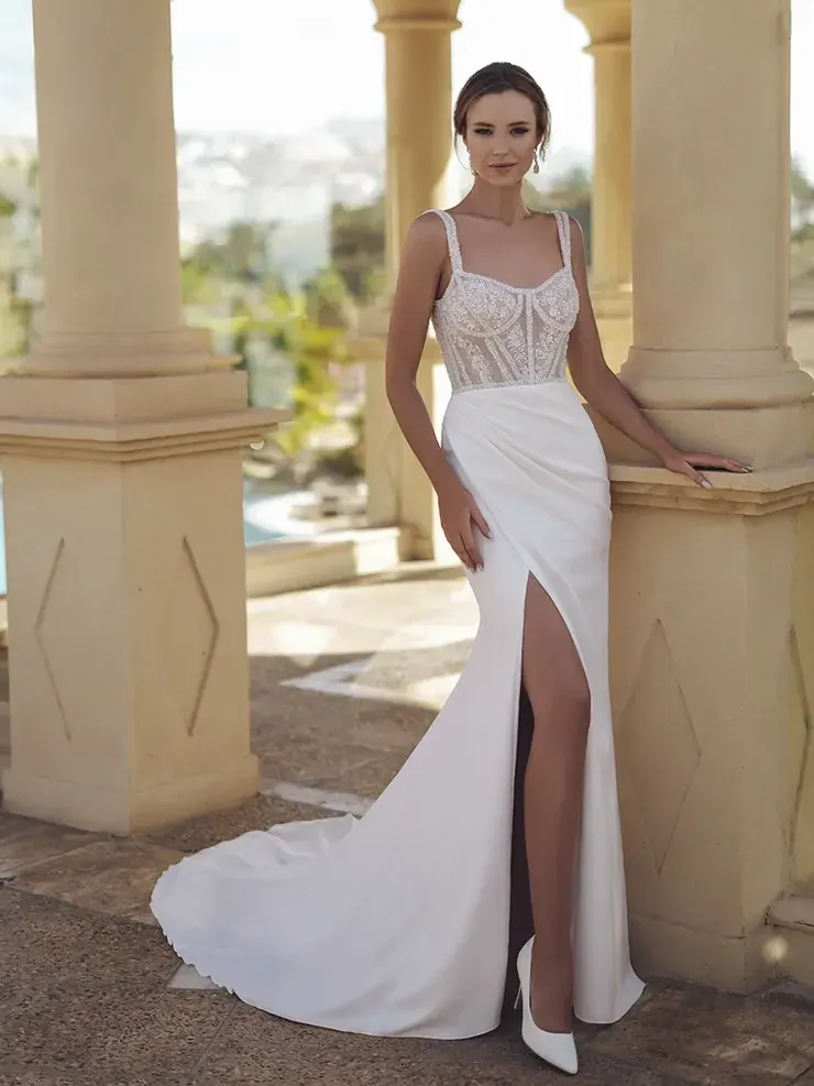 A woman in a white dress with a high slit is standing next to a pillar.