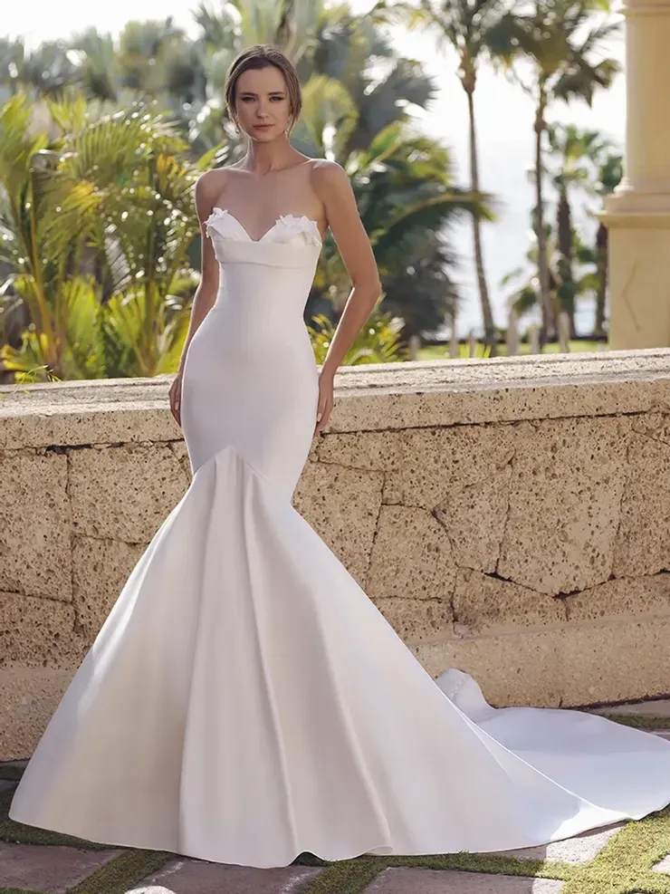 A woman in a white wedding dress is standing next to a stone wall.