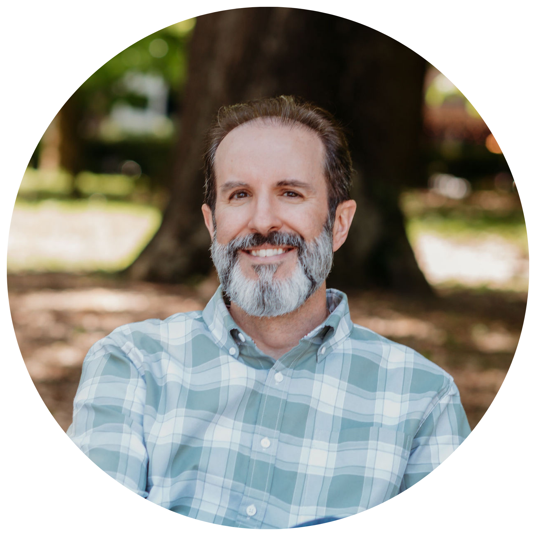 A man with a beard is sitting on a bench in a park.
