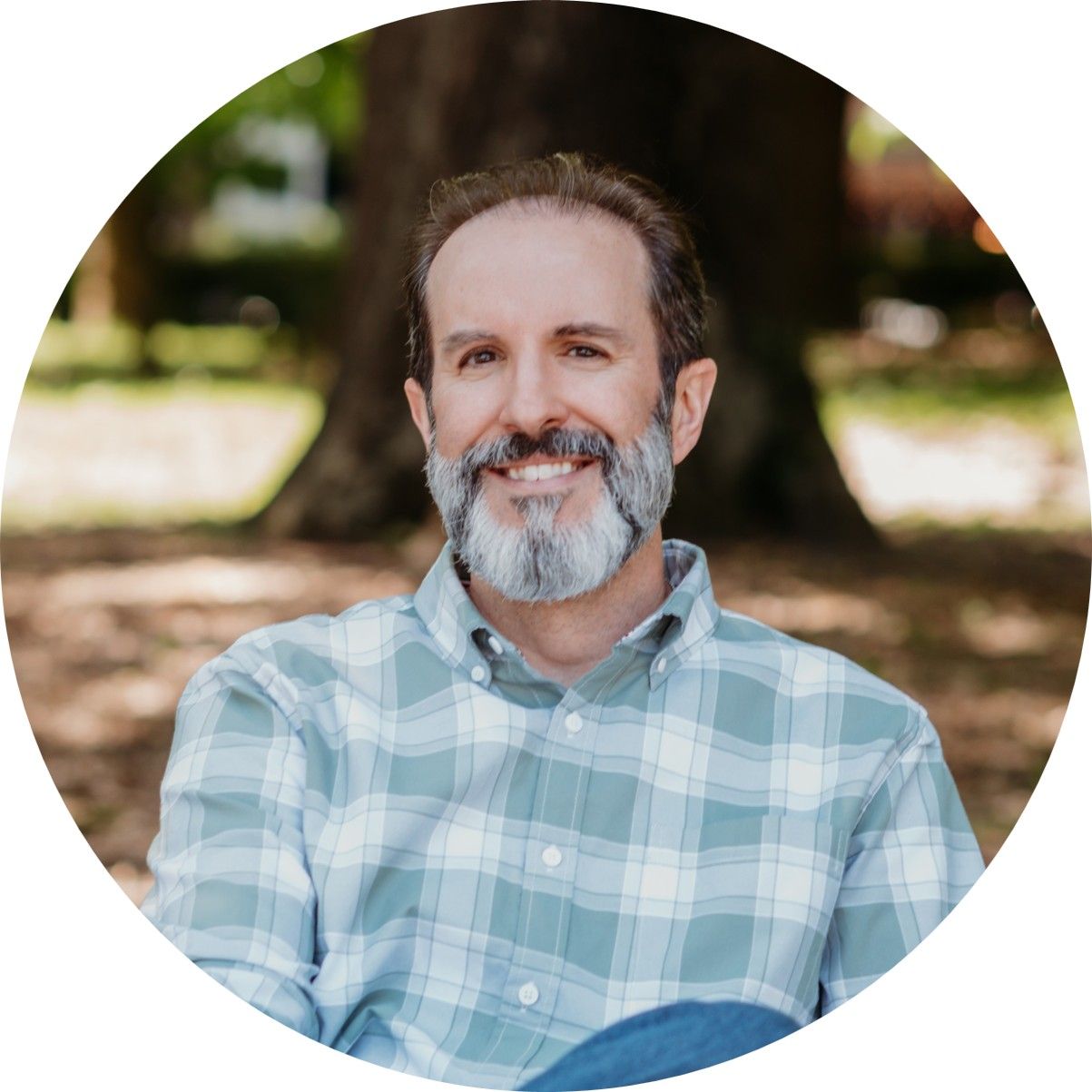 A man with a beard is sitting on a bench in a park.