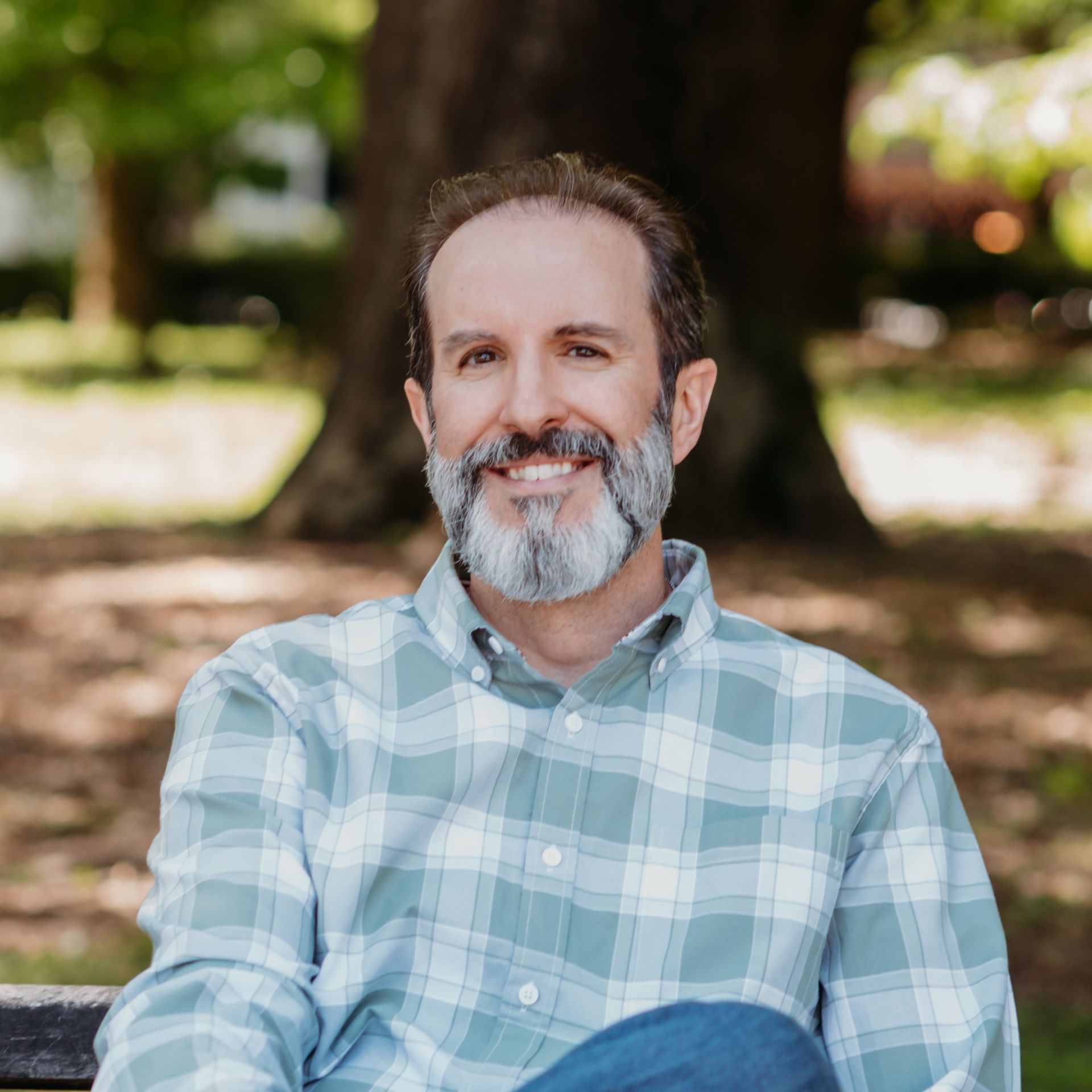 A man with a beard is sitting on a bench in a park.