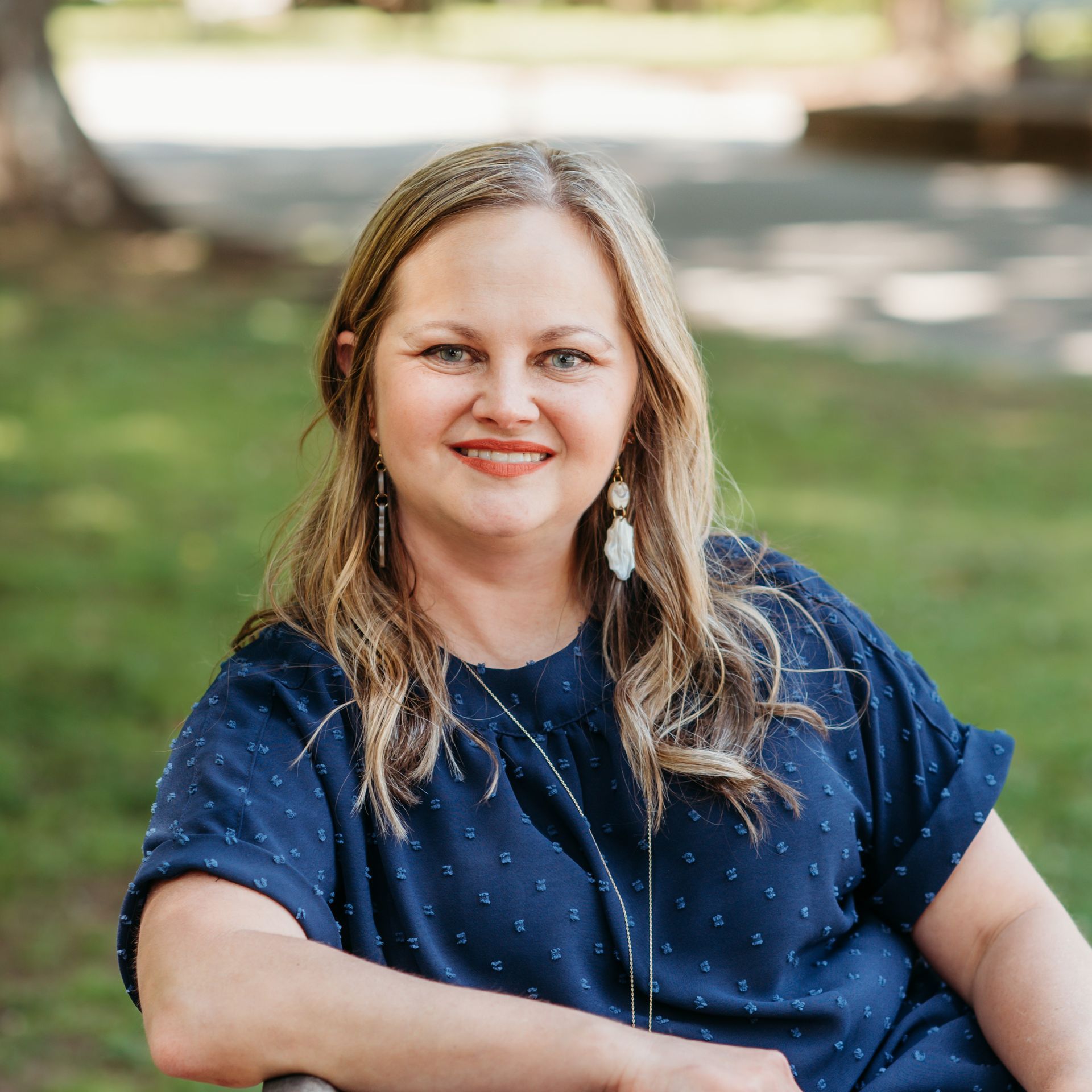 A woman in a blue shirt is sitting on a bench in a park.