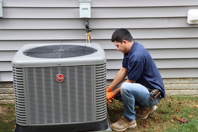 Air conditioning unit next to a brick wall and bushes on a lawn.
