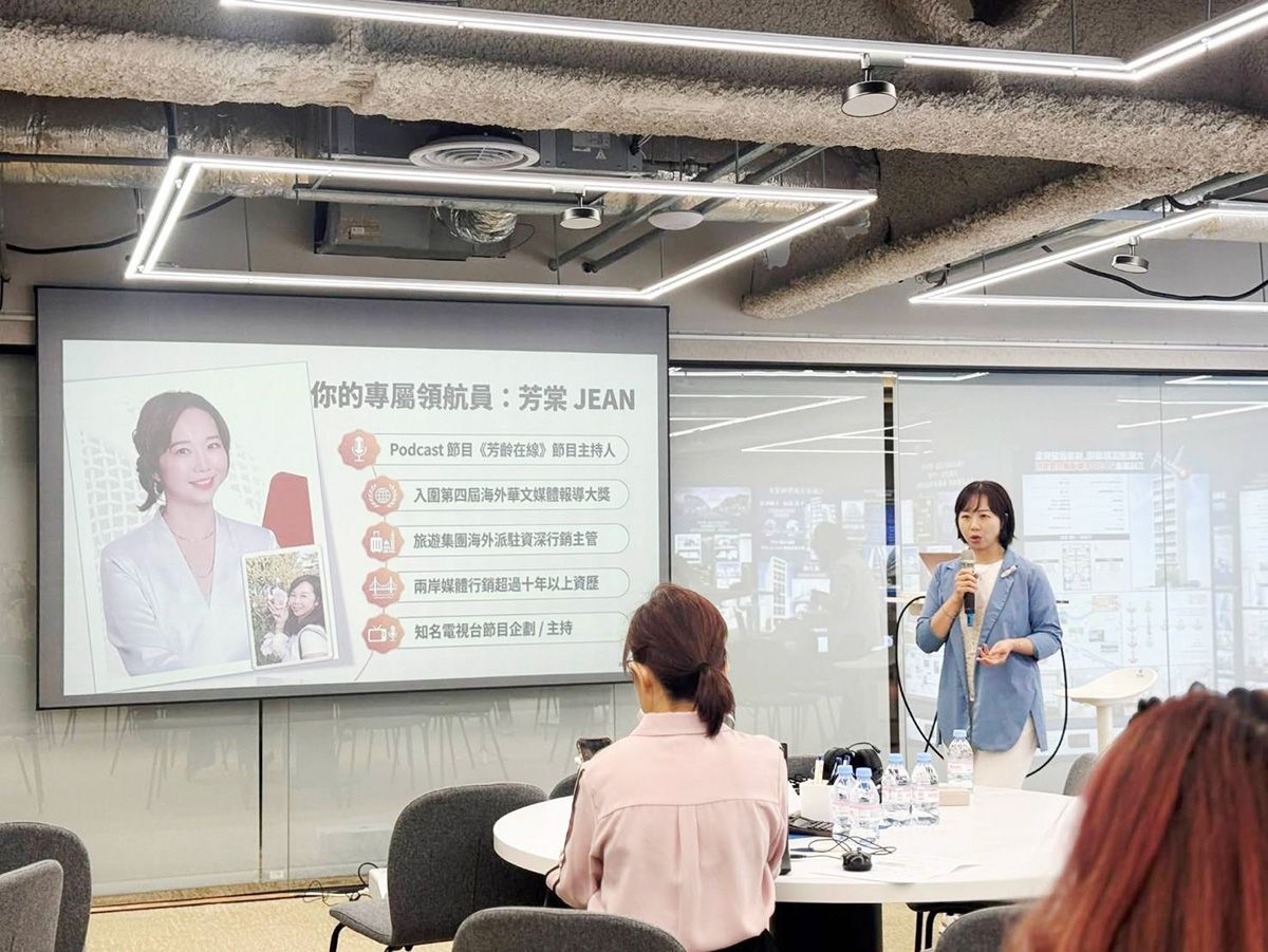 講者在會議室中發言，旁邊的投影畫面上顯示著一張肖像照和幾個重點項目。