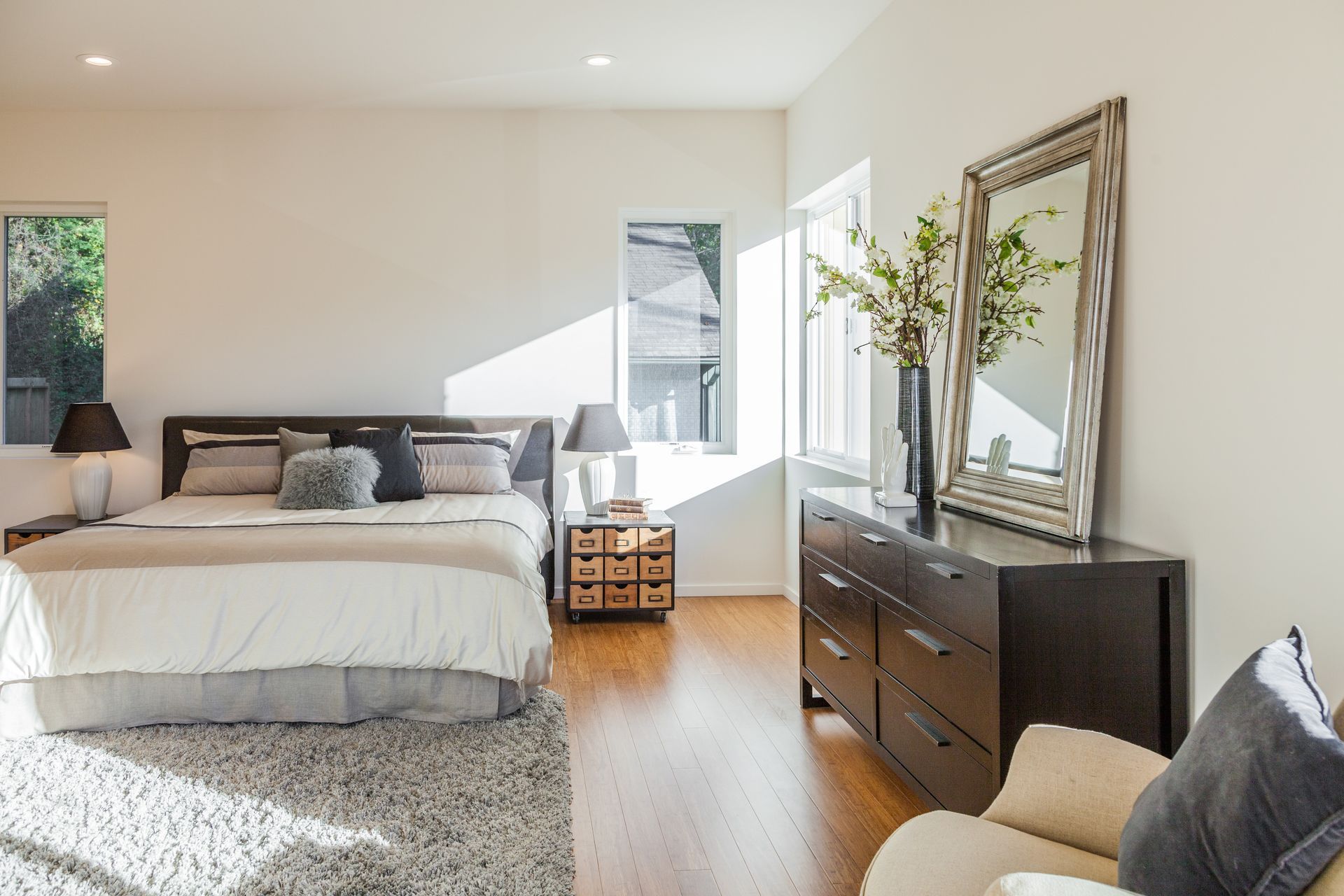 A bedroom with a large bed , dresser , chair and mirror.