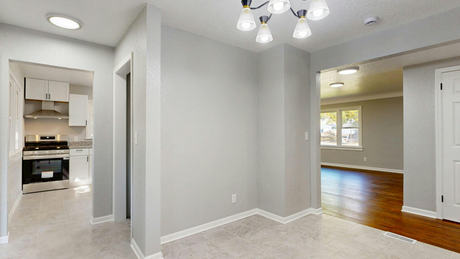 Bright empty home interior with gray walls, carpeted dining area, hardwood floor, and open kitchen doorway