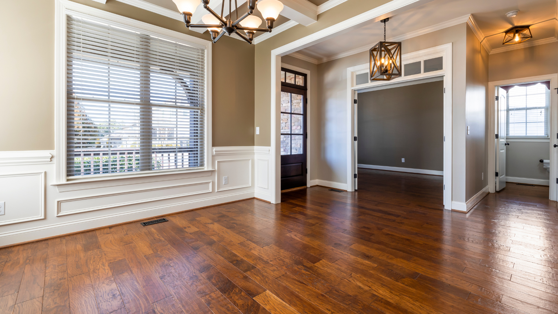 Empty dining room with hardwood floors, white wainscoting, and large windows with blinds.