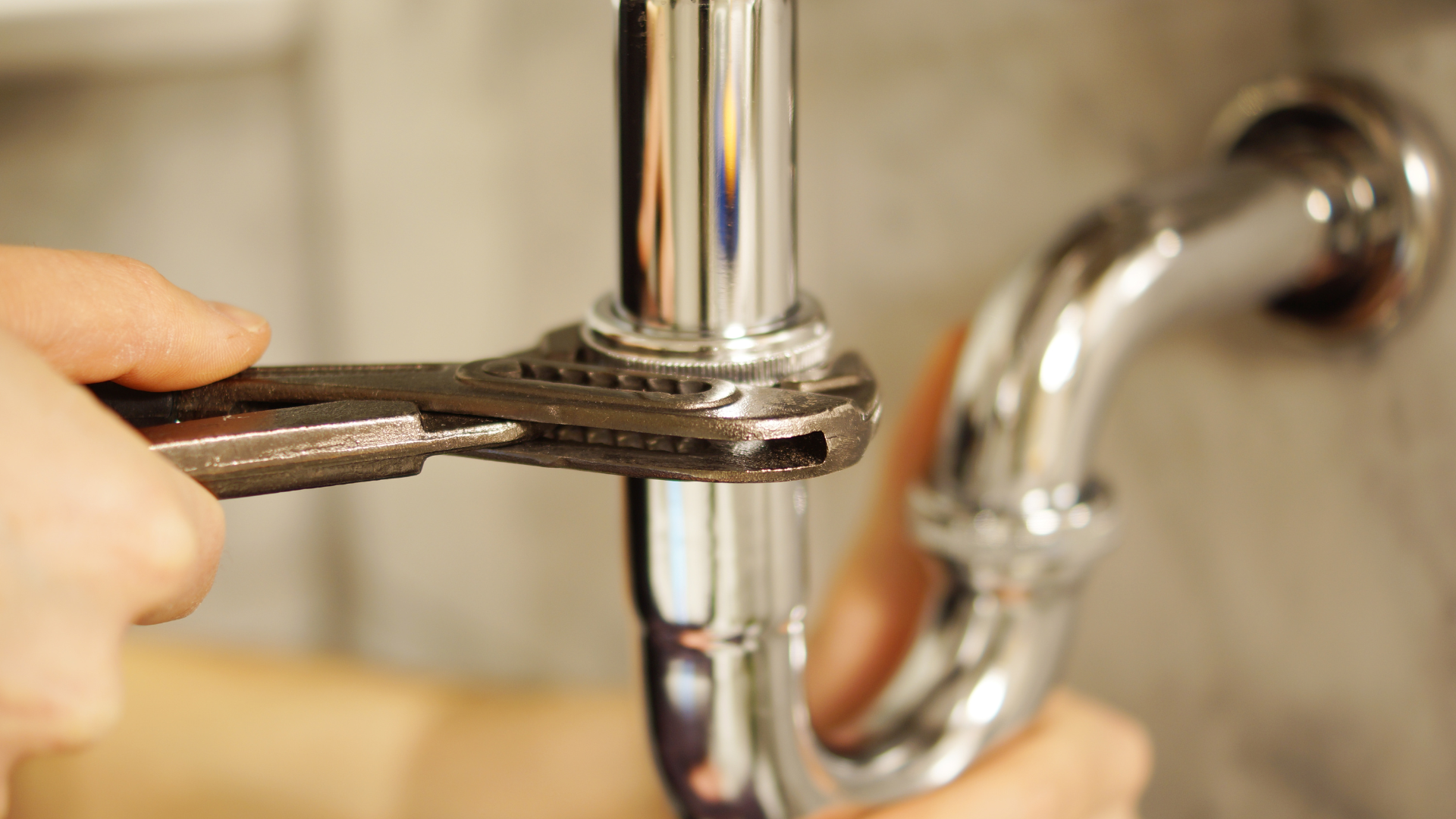 Hand tightening a chrome pipe fitting with a wrench under a sink