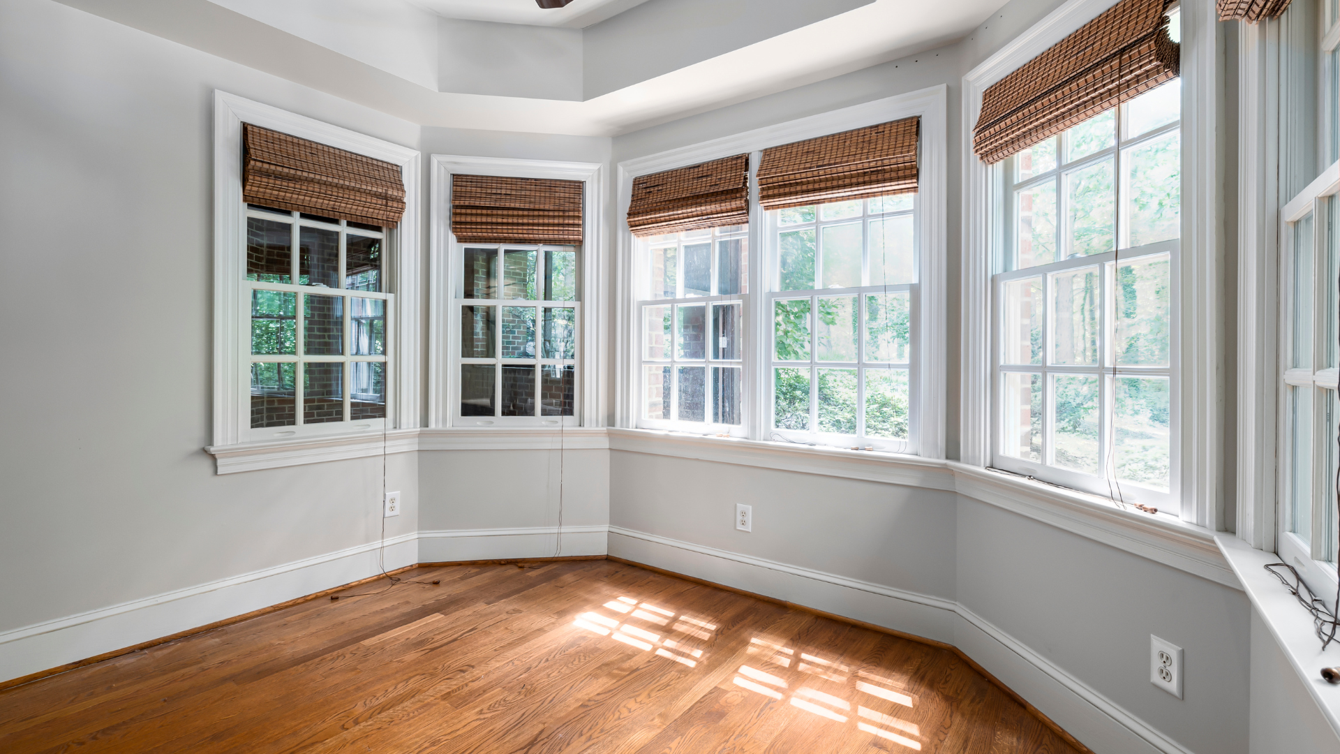 Bright empty sunroom with bay windows, white trim, wood blinds, and hardwood floor