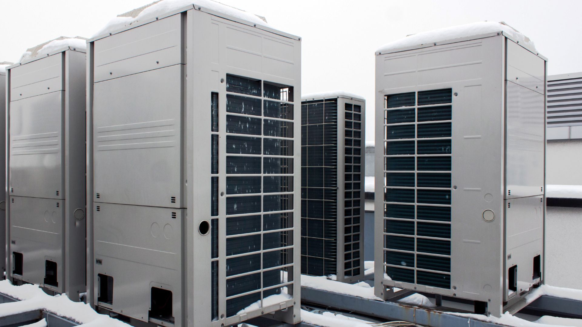 A row of air conditioners sitting on top of a building covered in snow.
