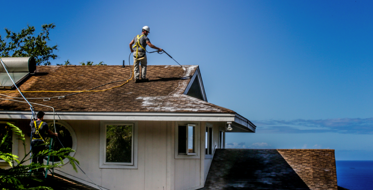 A man is cleaning the roof of a house with a high pressure washer.