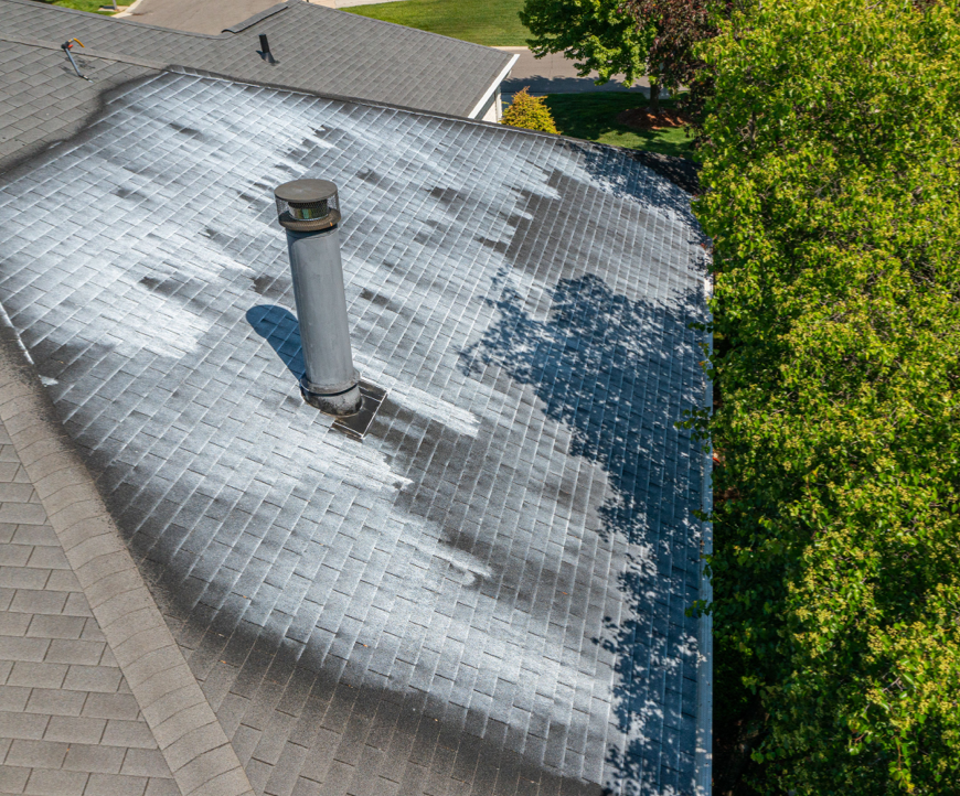 An aerial view of a roof with a chimney and trees in the background.