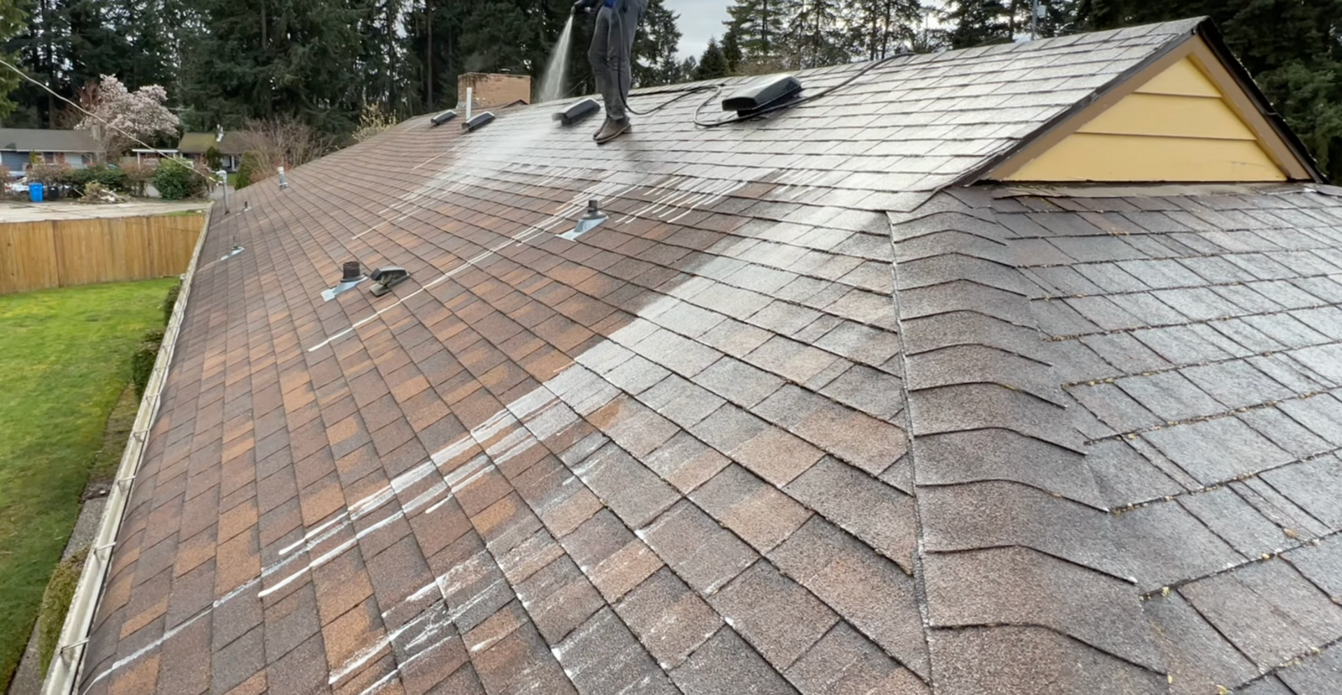 A man is cleaning the roof of a house with a pressure washer.
