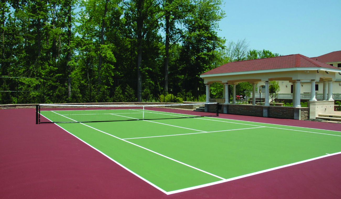 Tennis court with green playing surface and red surround, gazebo in background. Sunny day. Tennis court with green playing surface and red surround, gazebo in background. Sunny day.
