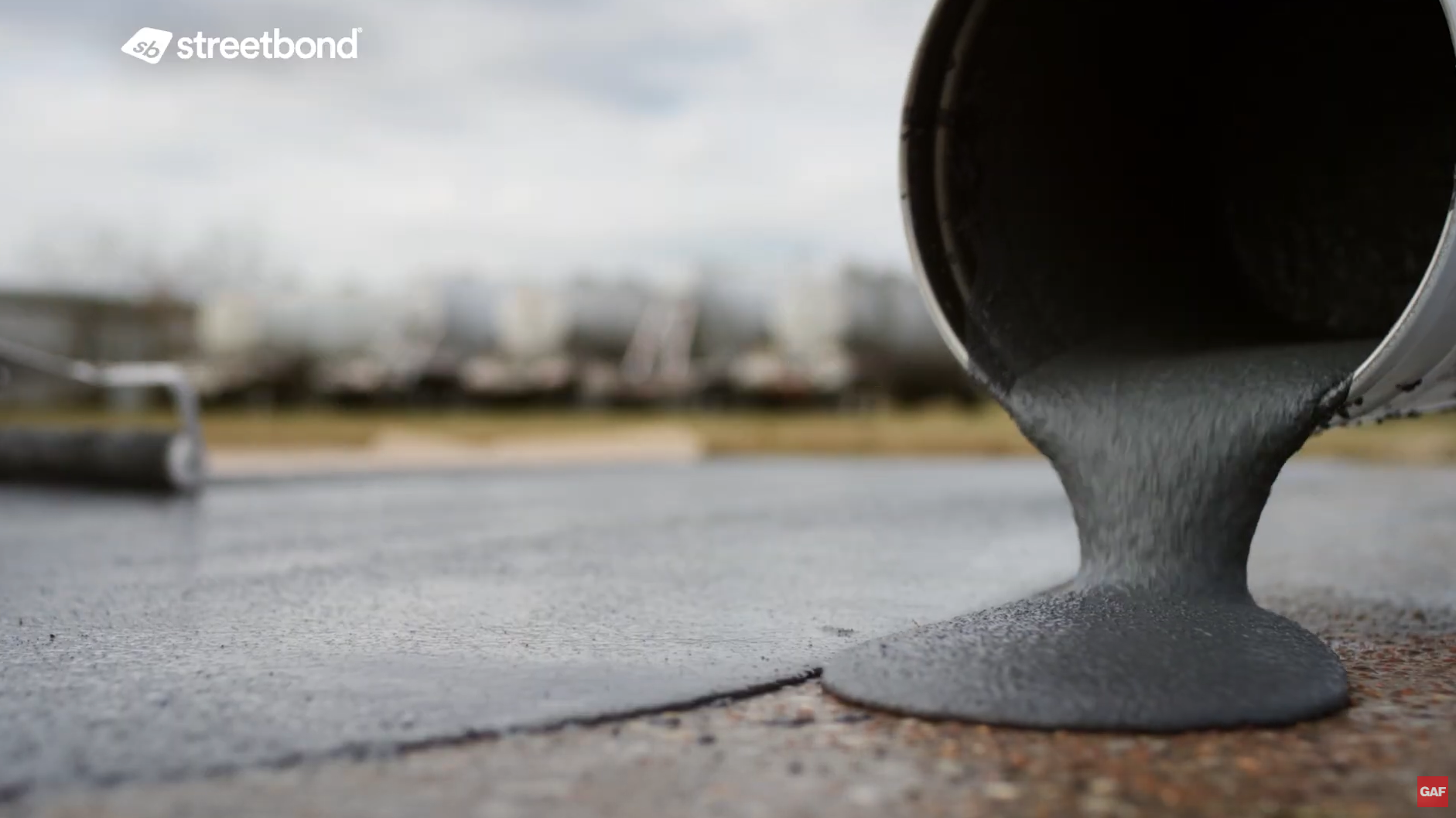 Gray liquid concrete pouring from a metal container onto a paved surface outdoors. Gray liquid concrete pouring from a metal container onto a paved surface outdoors.