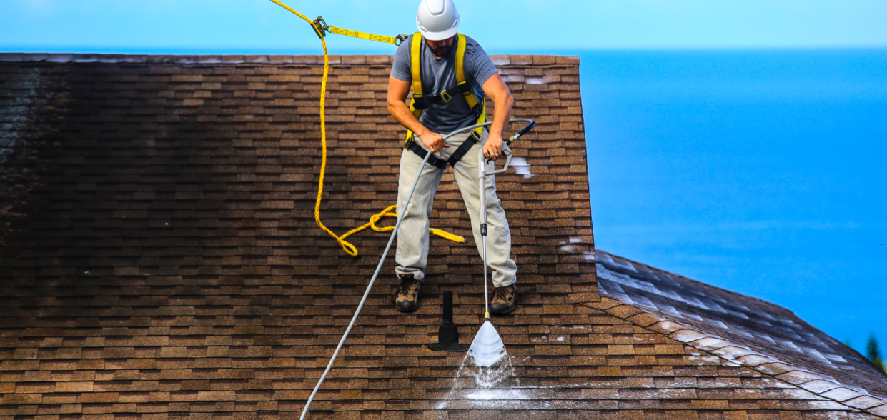 A man is cleaning a roof with a pressure washer.