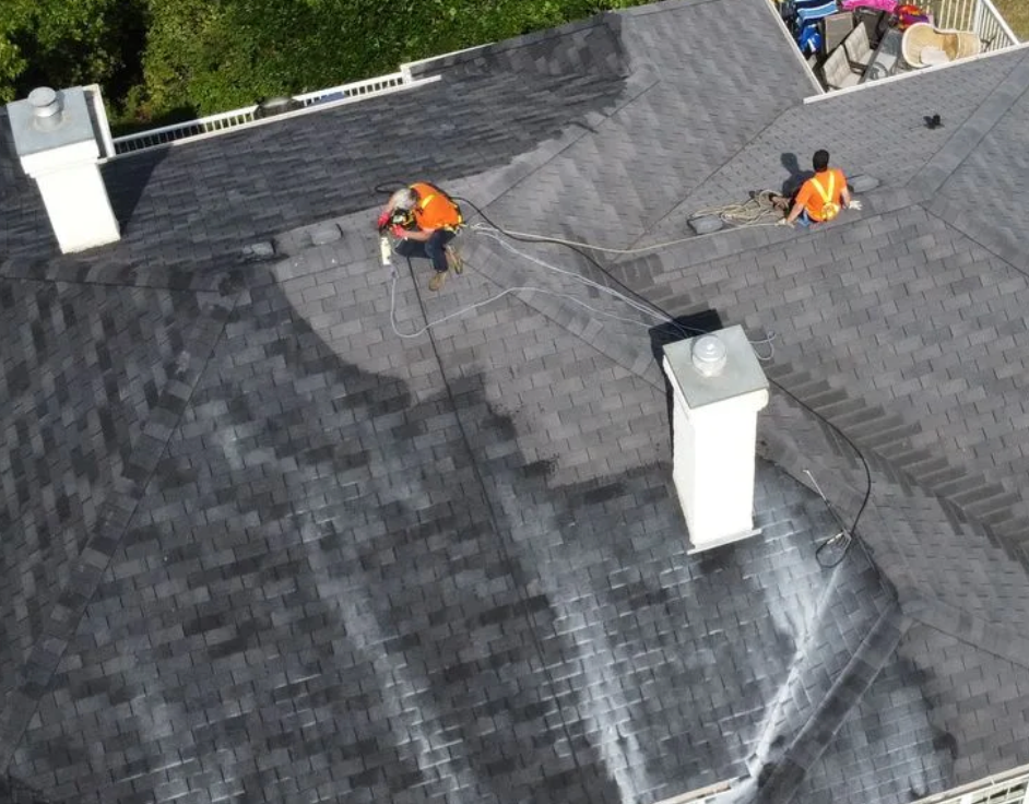 Two men are cleaning the roof of a house with a hose.