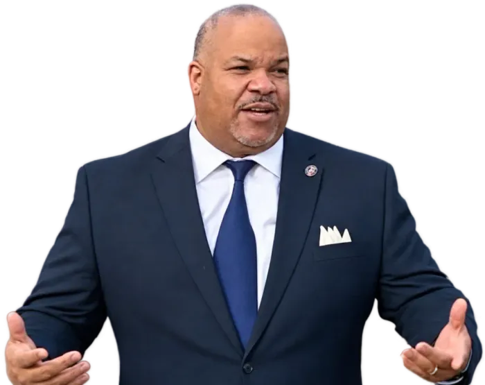 Man in navy suit speaking with hands open against a white background
