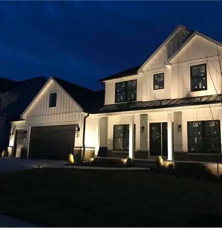 Well-lit white suburban house with black trim at dusk, showing a two-car garage and front porch.