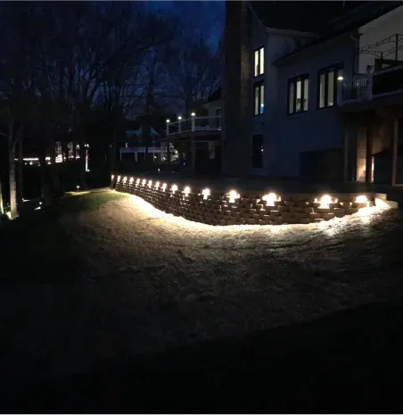 Nighttime path lit by small lights beside a building, with trees in the background
