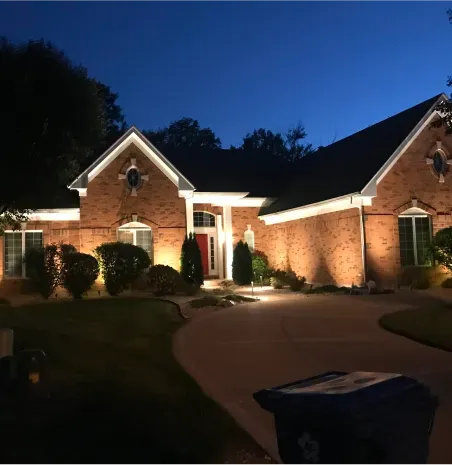Brick house lit at dusk with a curved driveway and landscaped front yard