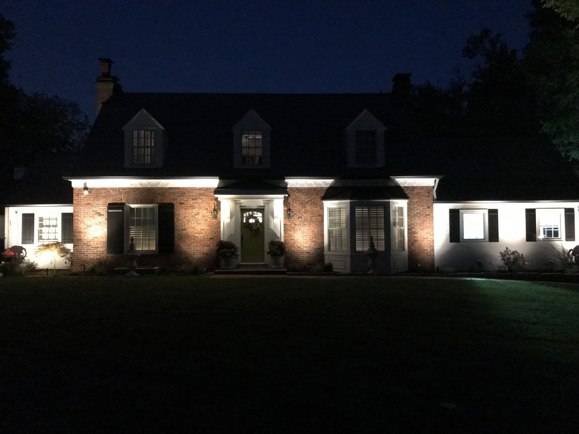 Nighttime view of a lit brick house with white wings and a dark front lawn
