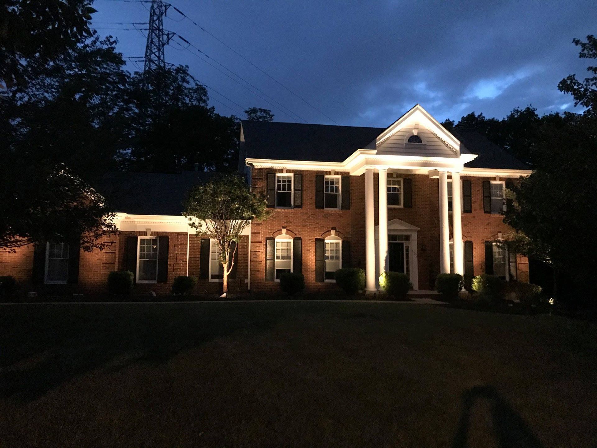 Brick house at dusk with bright porch lights and tall white columns in front.