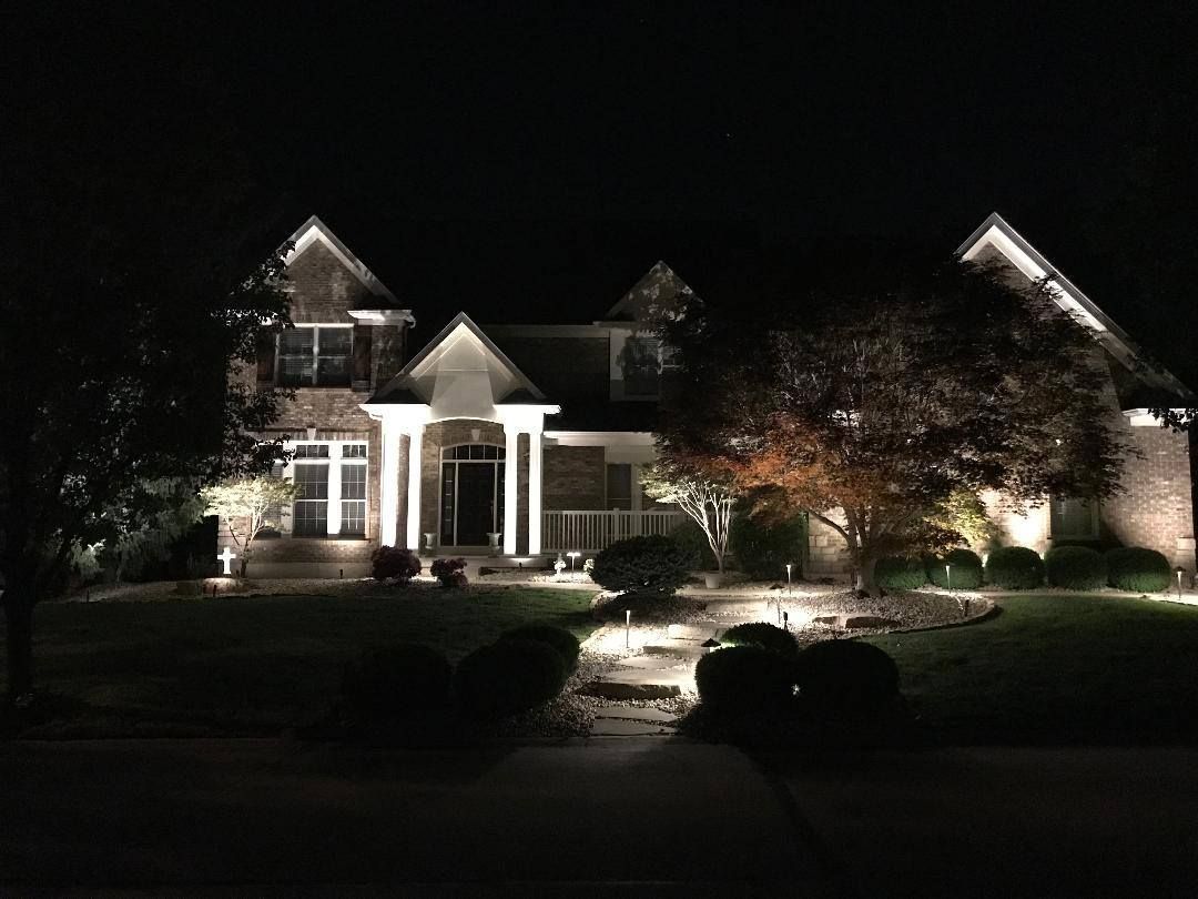 Illuminated suburban house at night with a landscaped front yard and trees