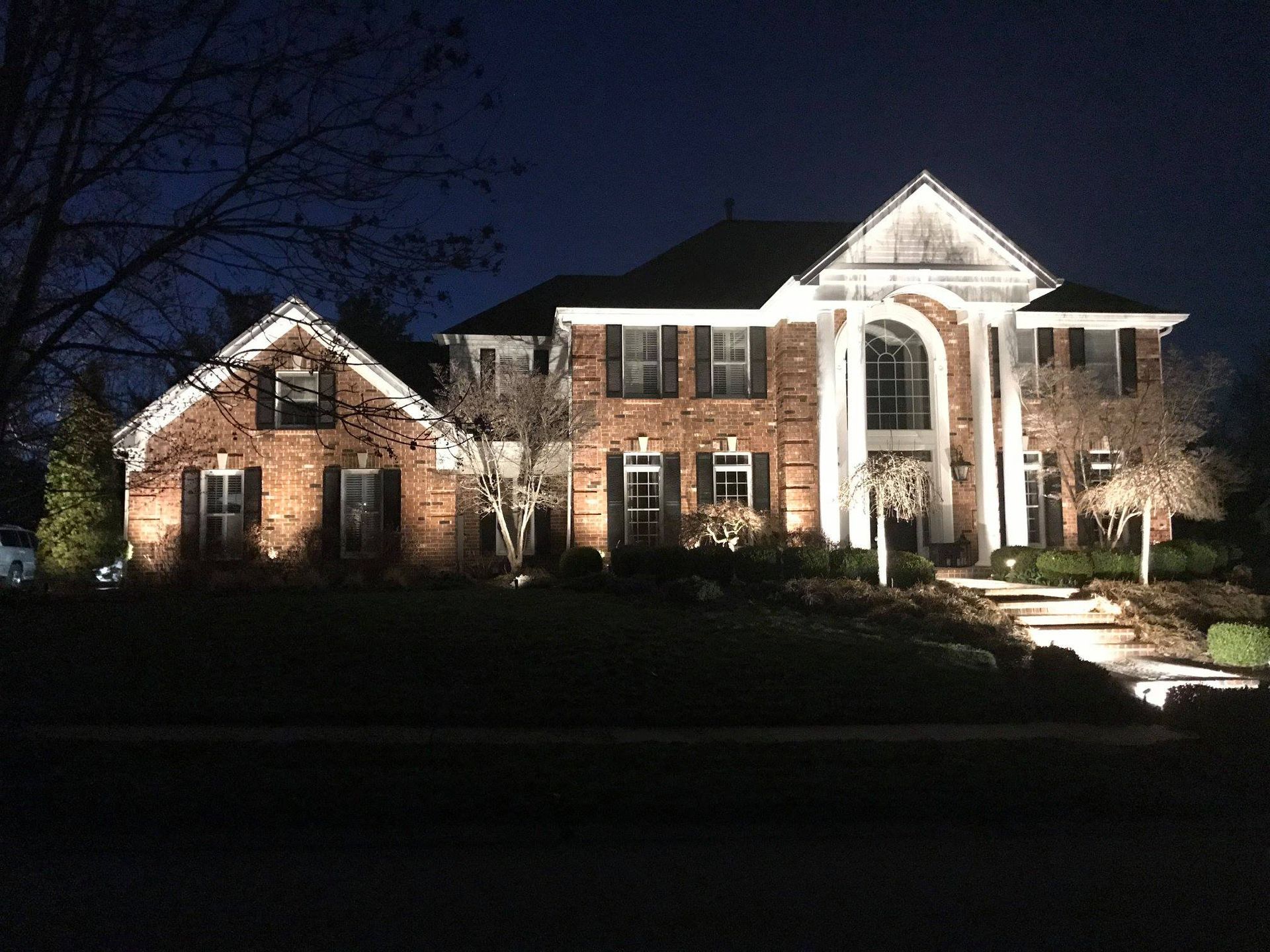 Outdoor patio with cushioned seating around a glowing fire pit at night, lit by warm ambient lights.