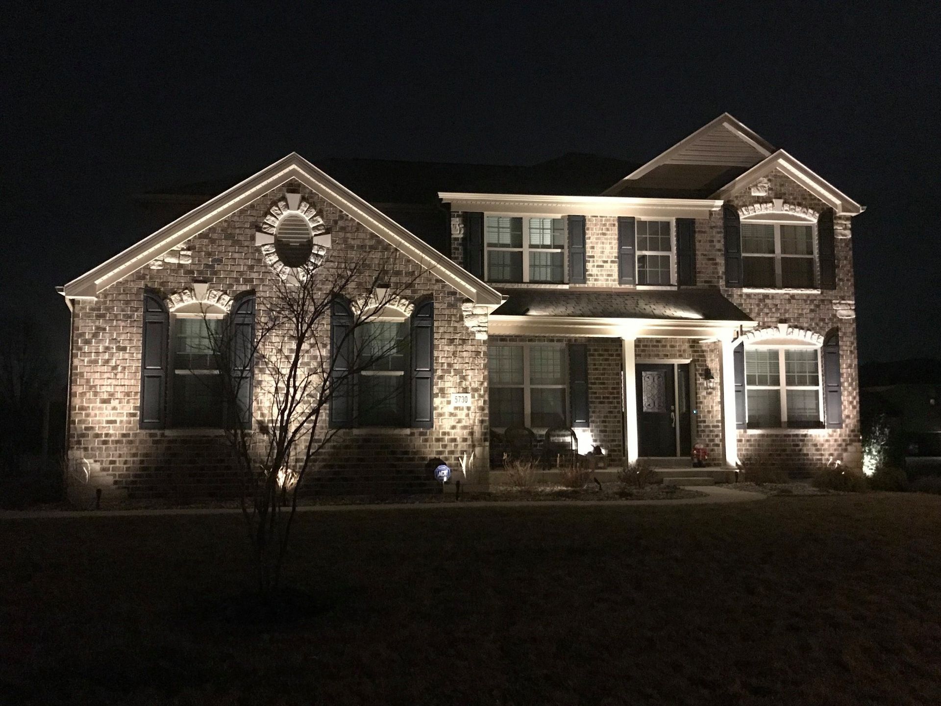 Stone house lit at night with white-trimmed windows and a front porch
