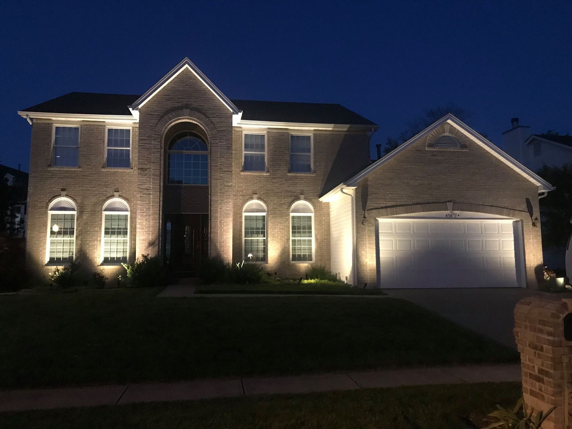 Large stone house at night, warmly lit with glowing windows, landscaped garden, and curved driveway