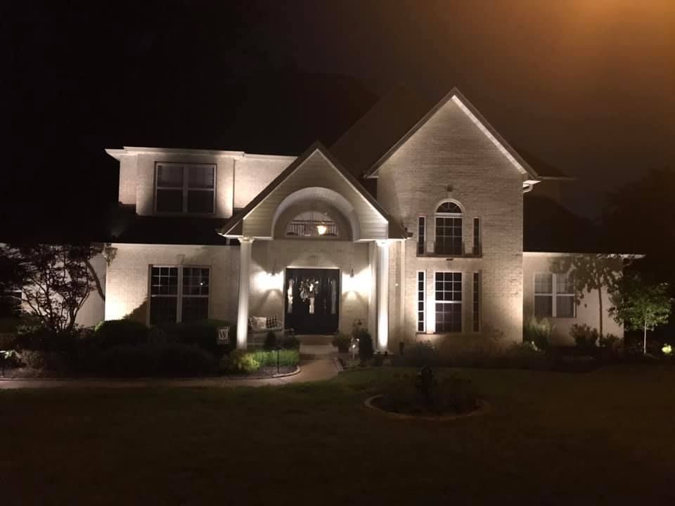 Lit house at night with bright exterior lights and a landscaped front yard