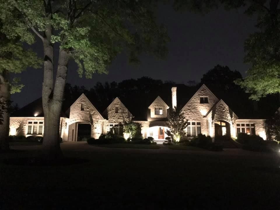 Large stone house lit at night, with glowing windows and trees framing the front lawn.