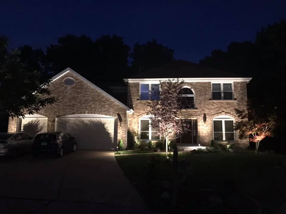 Illuminated two-story brick house at night with garage, driveway, and front yard lights